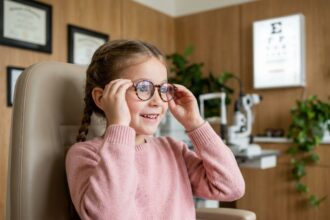 Petite fille essayant ses premières lunettes chez l'opticien avec une expression de surprise joyeuse